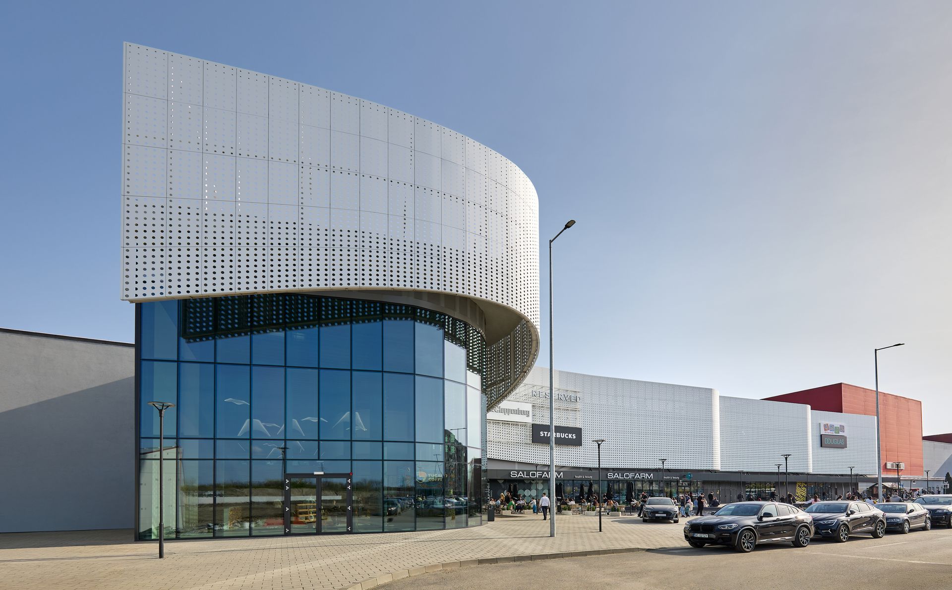Curved corner of the white volume of Arena Mall Bacău, next to the car park