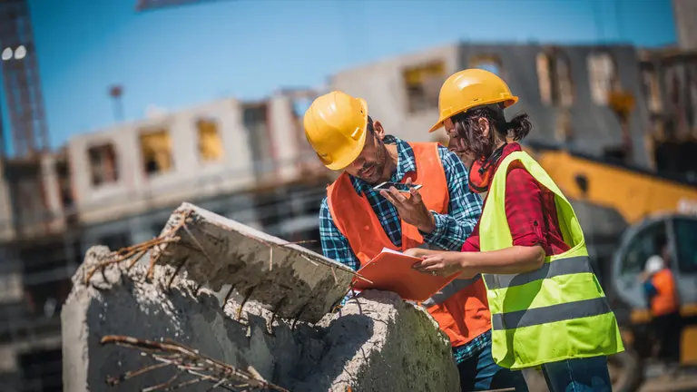 Two specialists in hard hats checking documentation on site, beside a precast concrete element