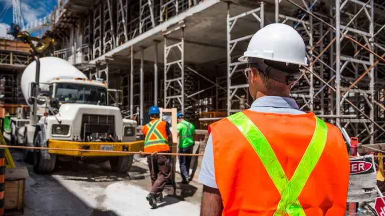 Site worker in helmet and hi-vis vest, with concrete mixer and formwork behind