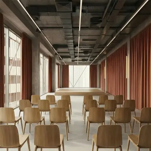 Sală de conferințe cu tavan din beton aparent, draperii în nuanțe de teracotă și scaune din lemn dispuse în fața unui ecran curbat.