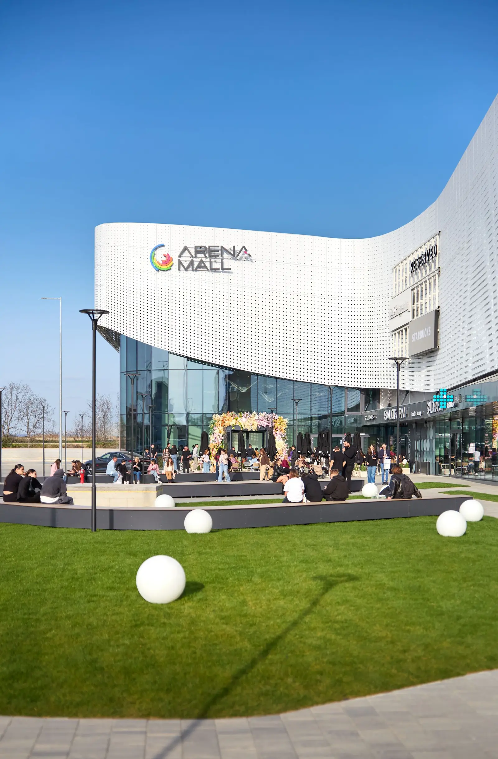 Intrarea principală și esplanada Arena Mall Bacău, cu vizitatori și elemente decorative sferice